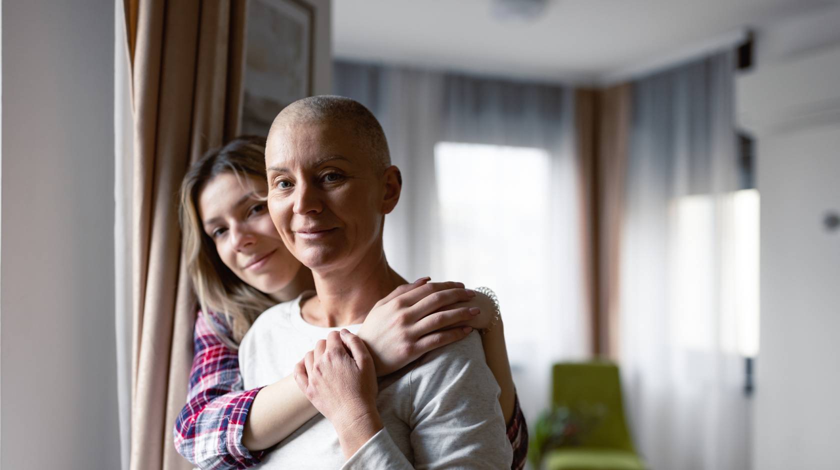 A grown child holds her mother, who has little hair on her head