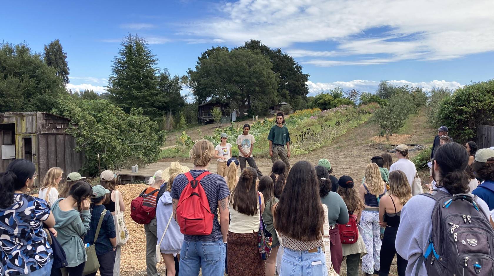 Two people speak to a small crowd of students in a garden