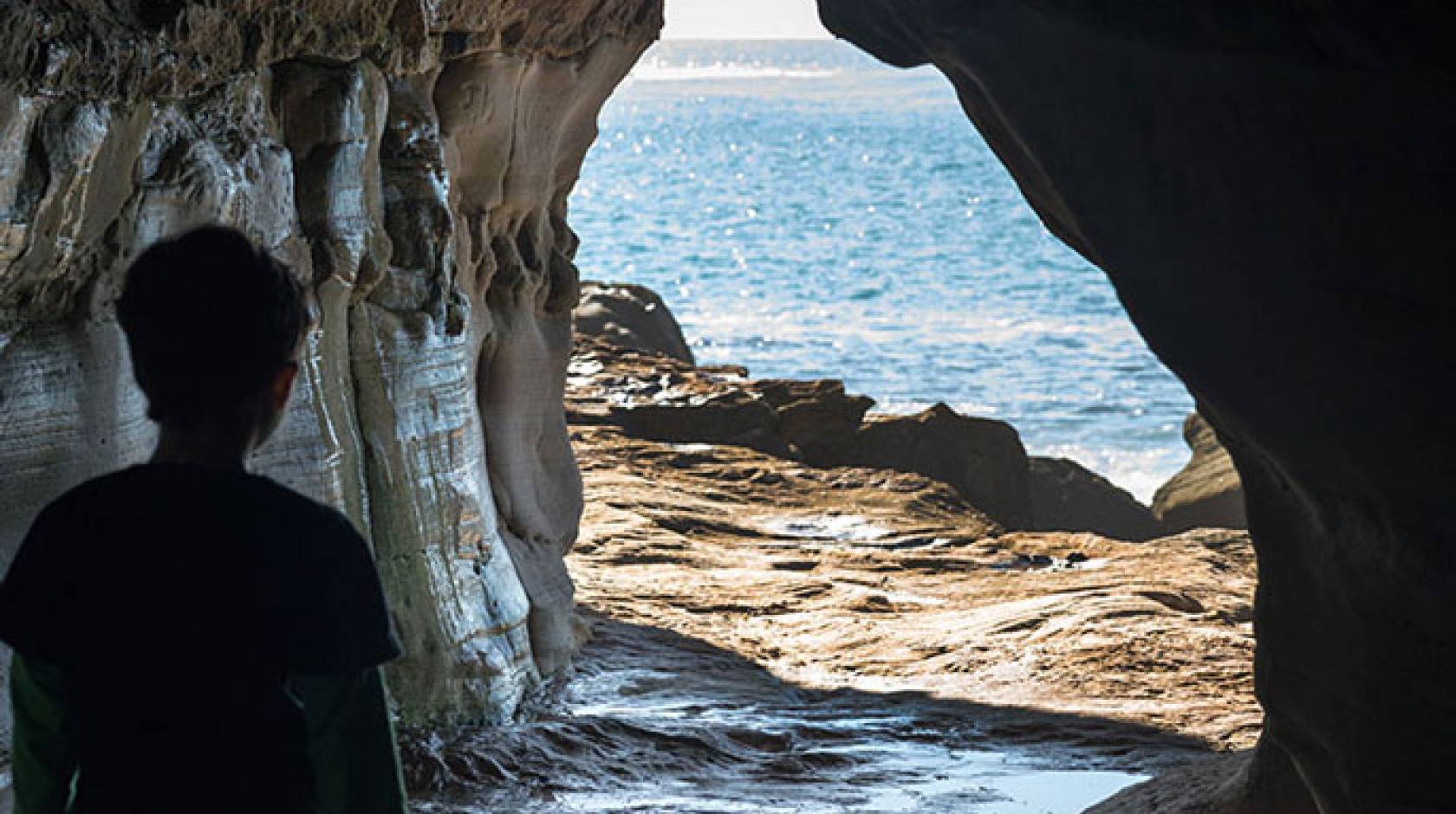 Person looking out from a cave at water