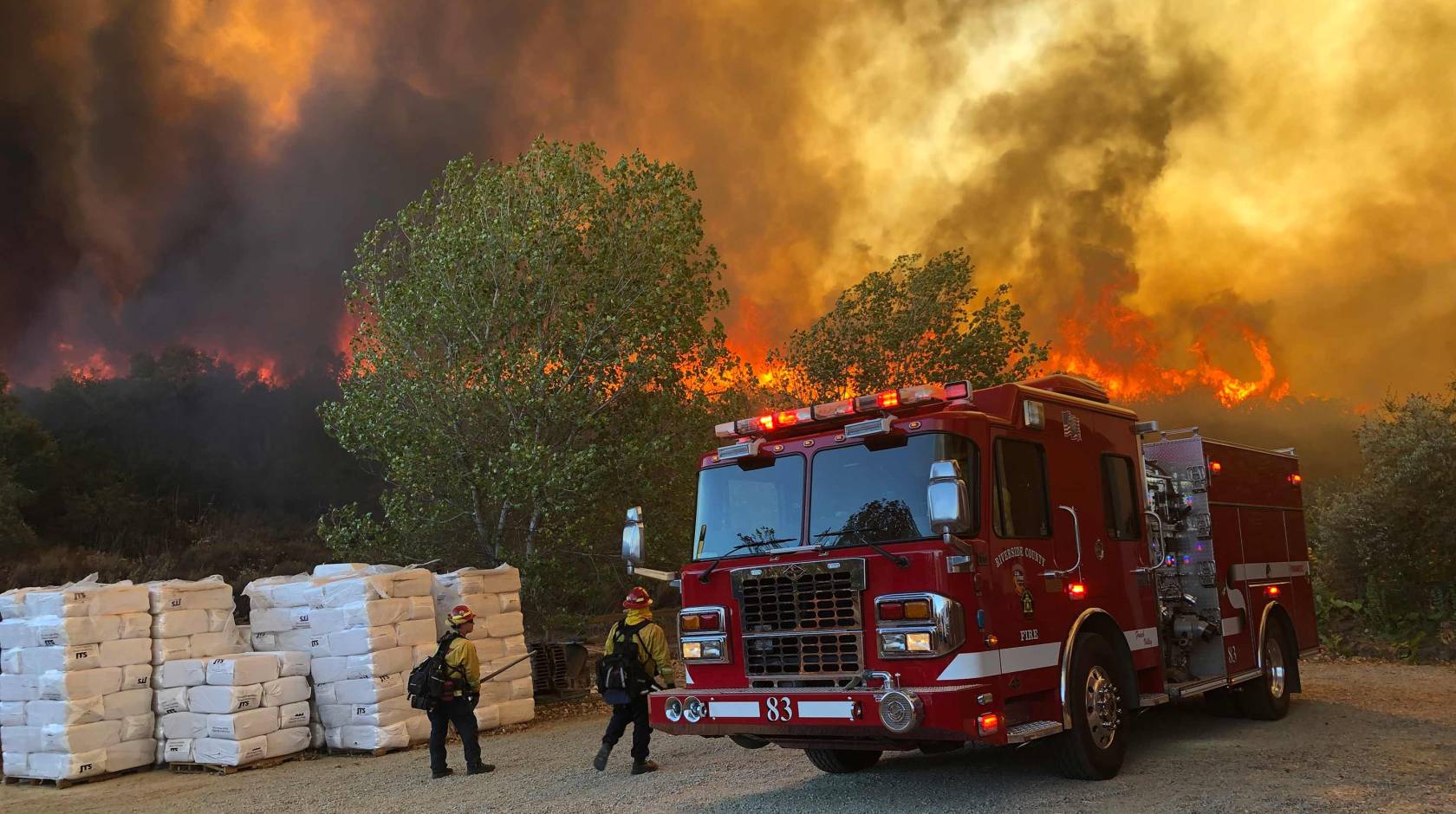 Fire truck and two firefighters with Chaparral fire behind