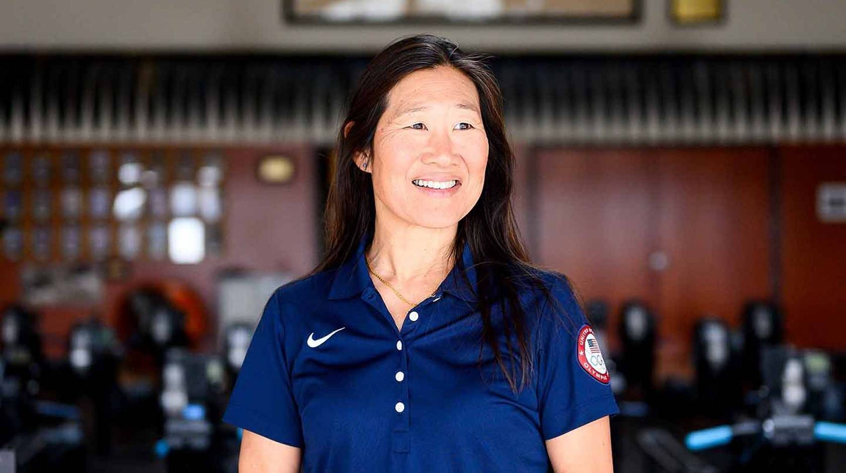 Dr. Cindy Chang poses for a portrait in front of a set of exercise equipment. In the background is a framed Olympic flag.