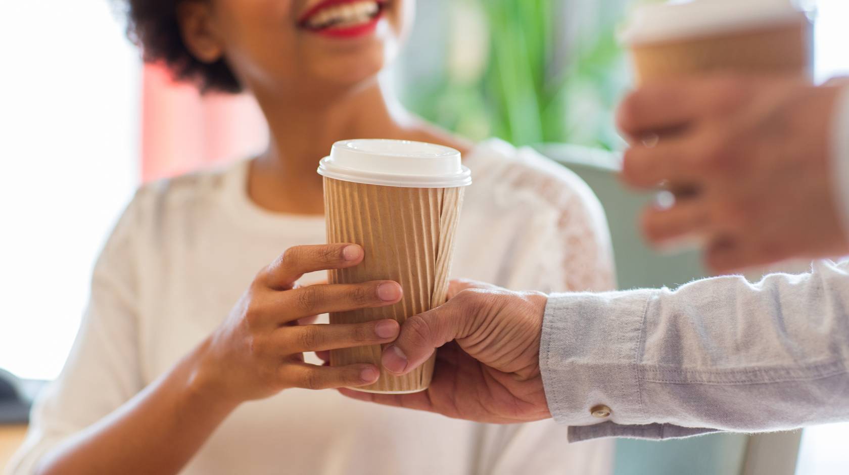 A person hands a smiling Black woman a to go cup of coffee