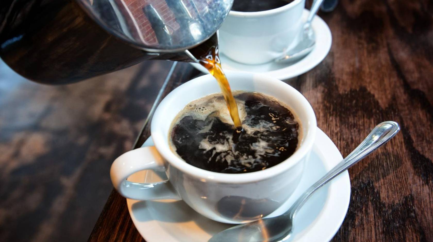 Coffee being poured into a cup, another cup behind it