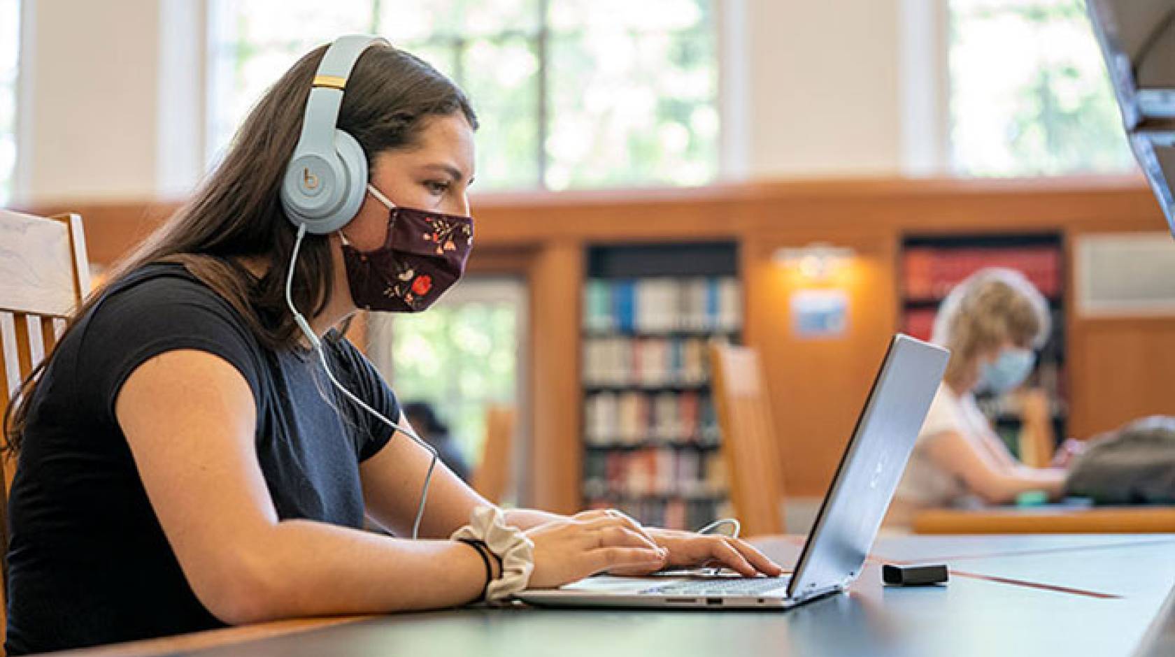 Young female student in mask at a library on computer