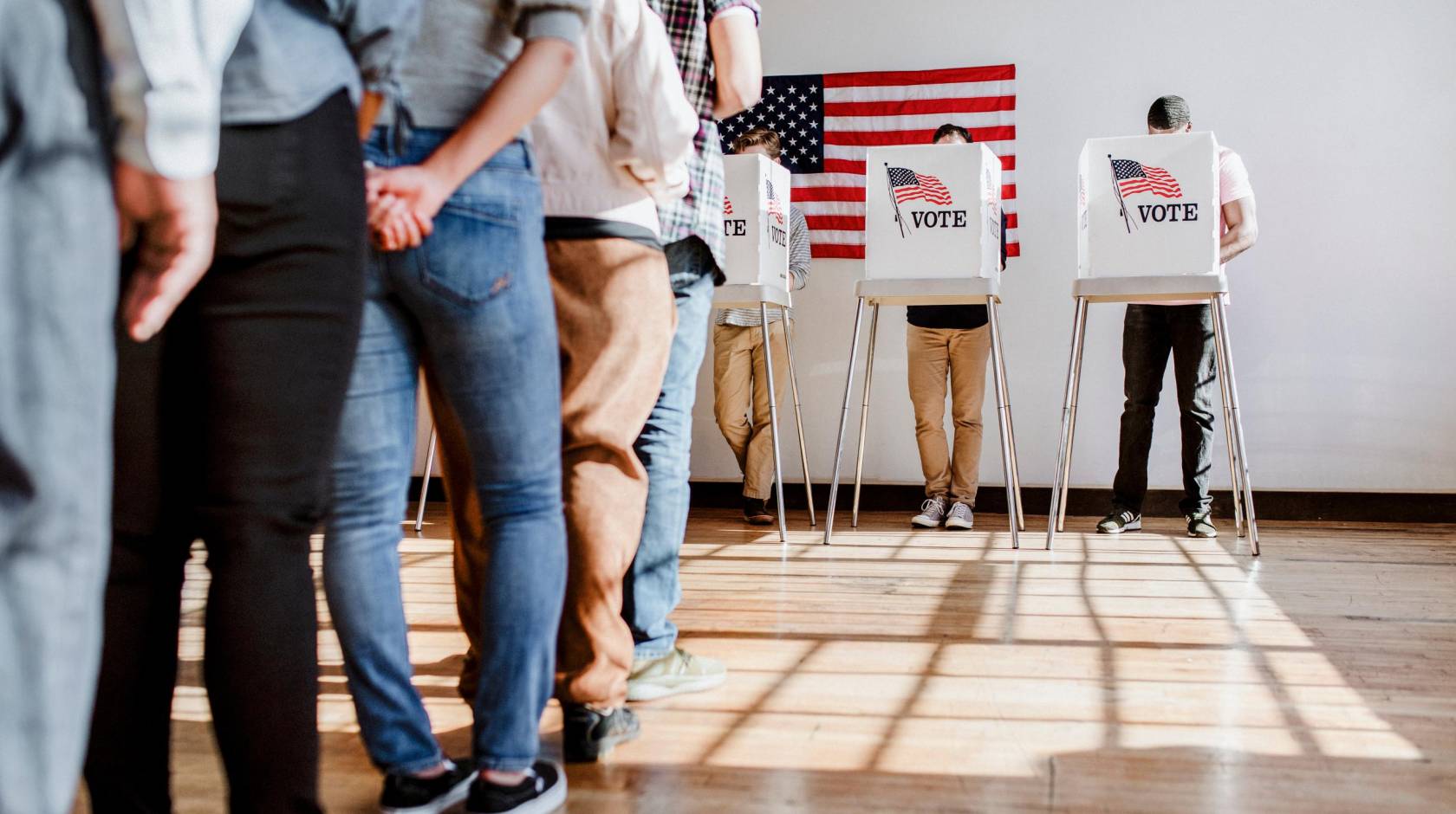 A line of people ready to vote and one person in a booth