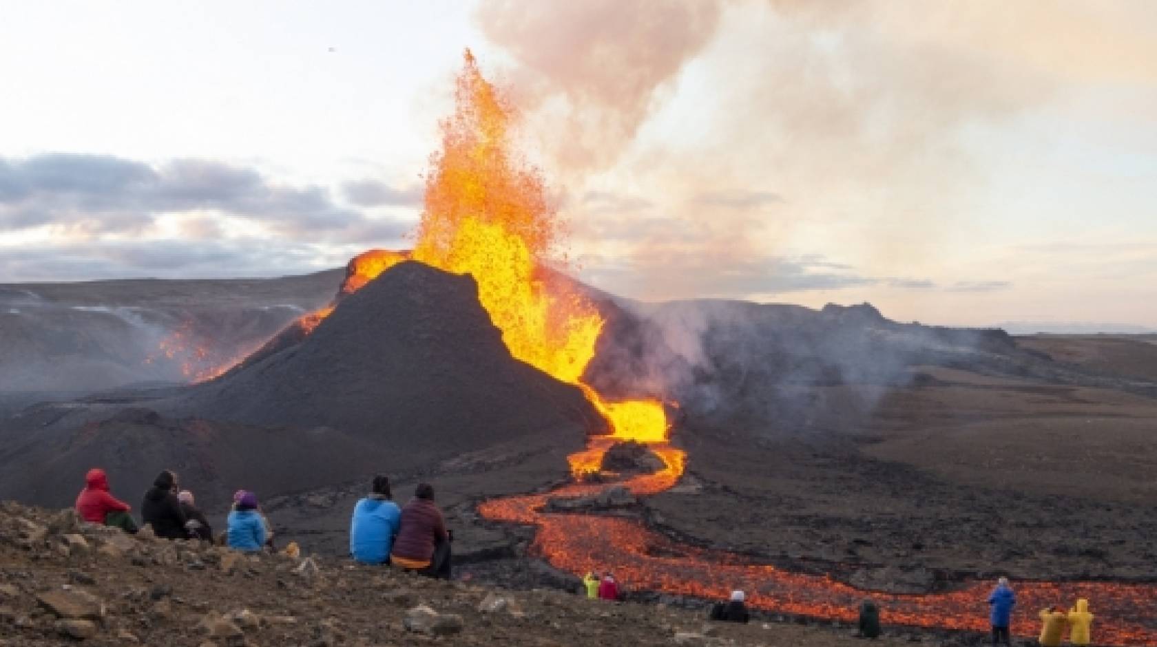 People sitting on a hillside watching Iceland’s Fagradalsfjall erupt