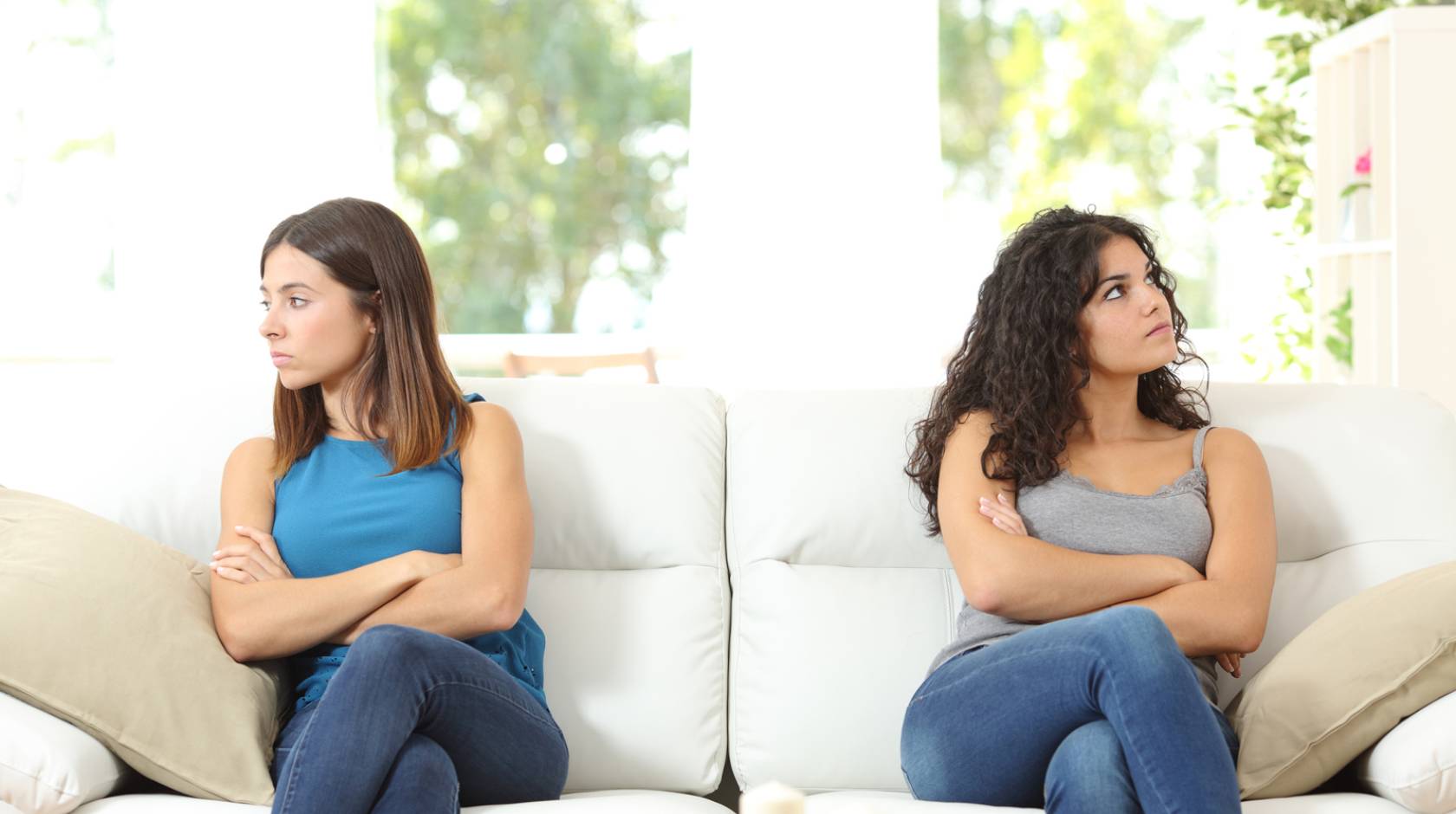 Young women on a couch looking away from each other, arms crossed