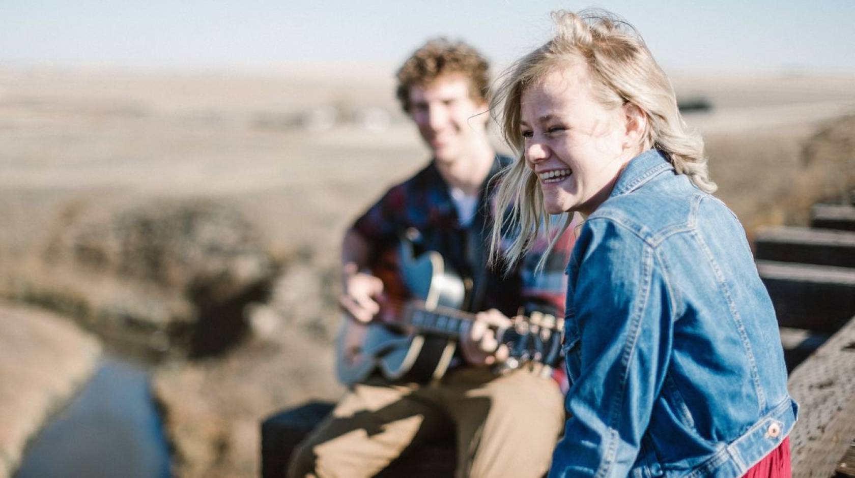 A happy woman smiling as she listens to a man play guitar