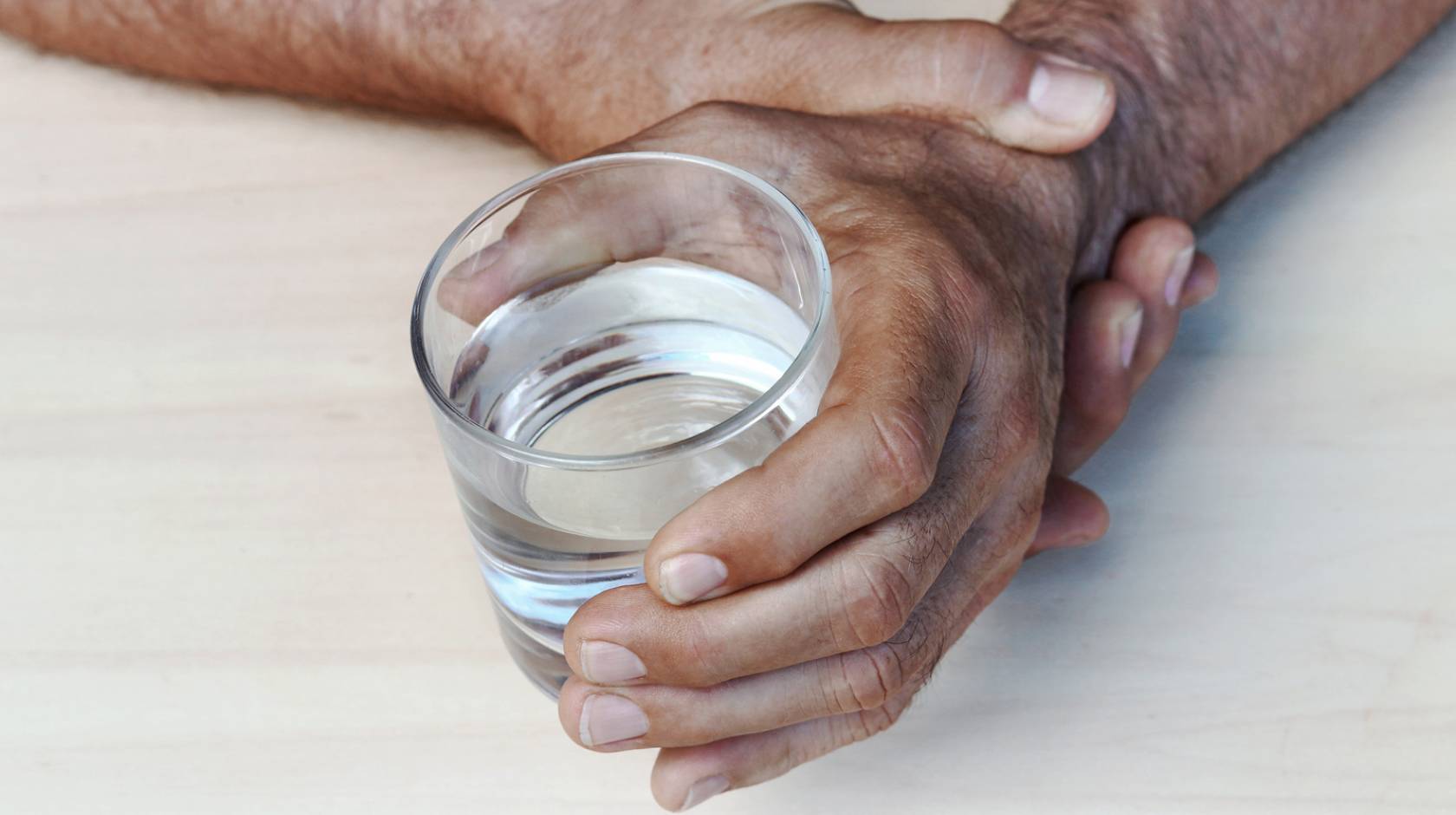 A man steadying a hand holding a glass of water with his other hand