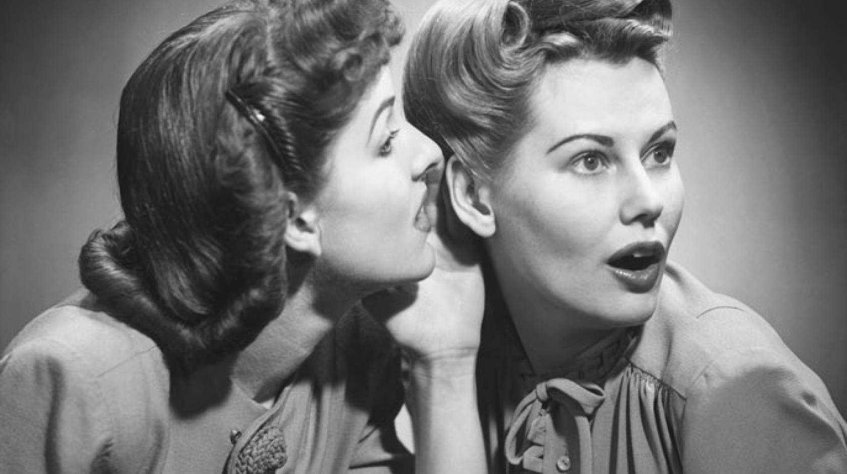 Two women in 50s hairstyles gossip in black and white photo