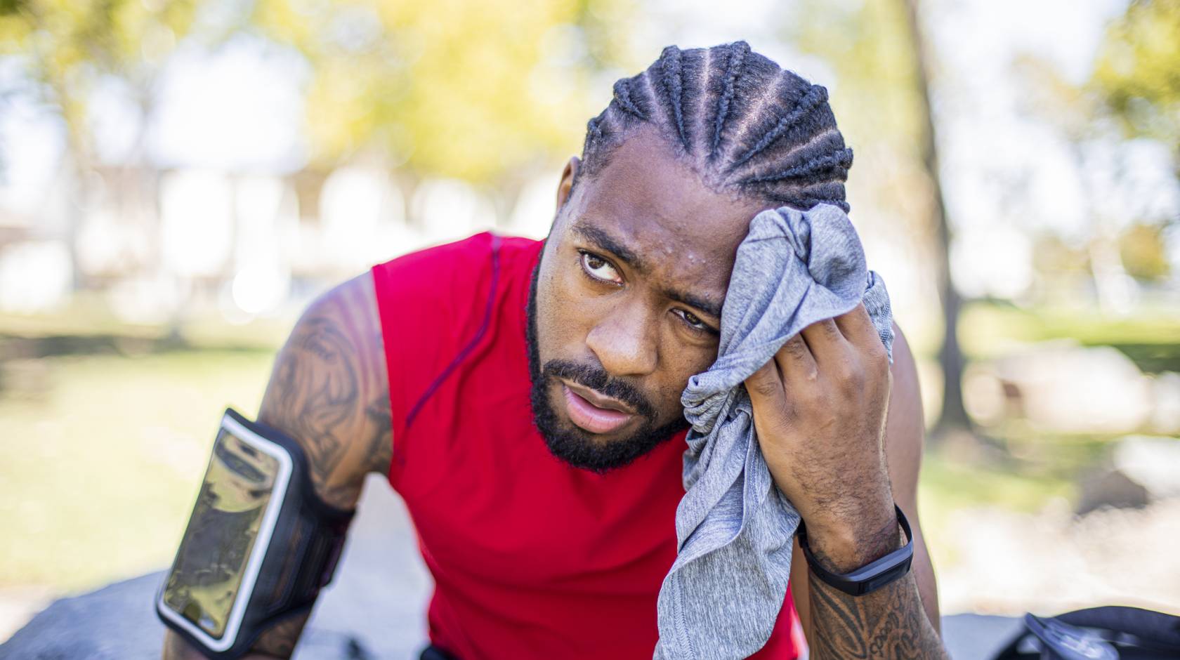 Young man wearing a phone on a sport band on his upper arm wipes sweat off his face and looks uncomfortable