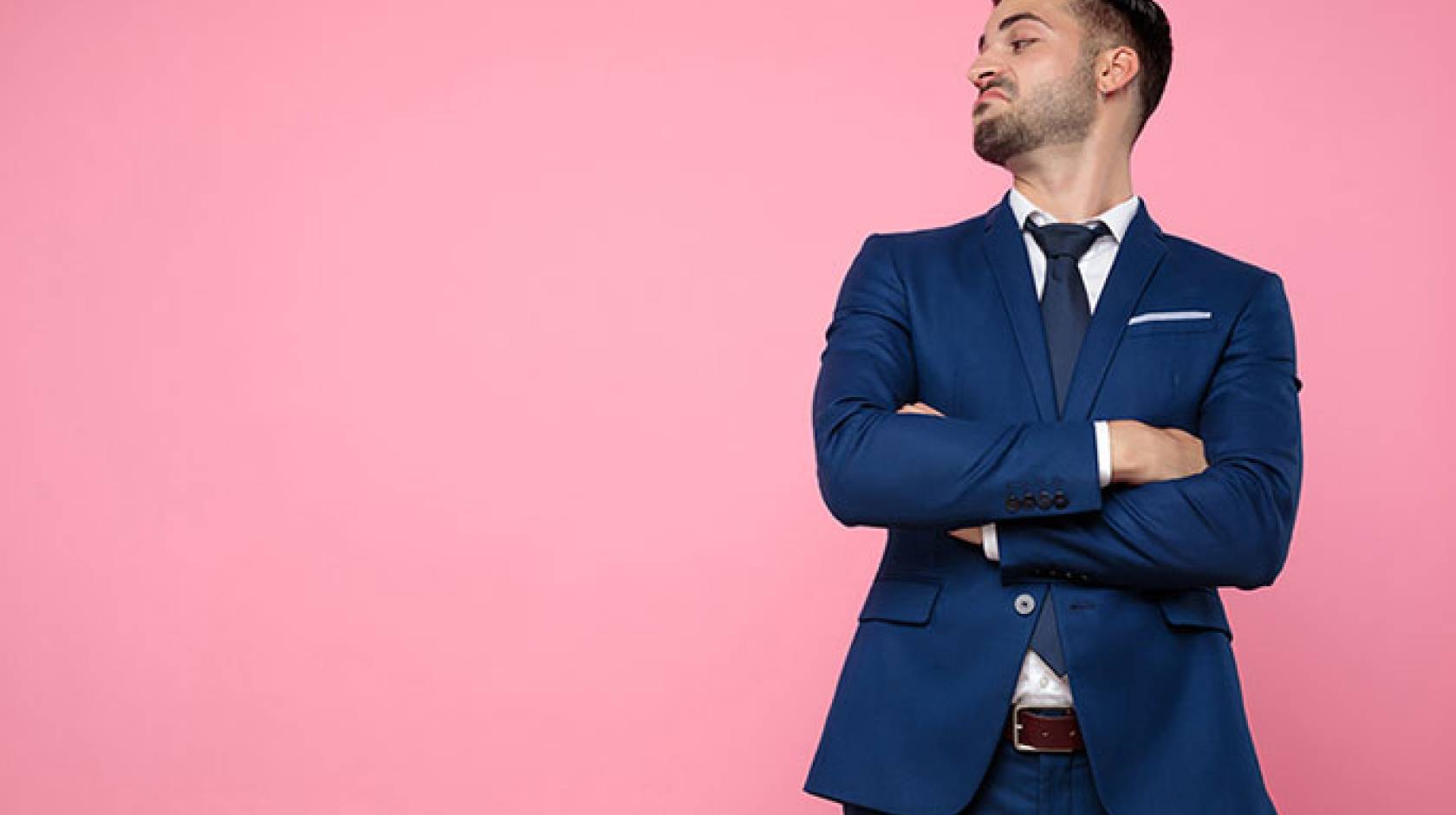 Man in tailored suit with arms crossed looking down with a hint of an attitude