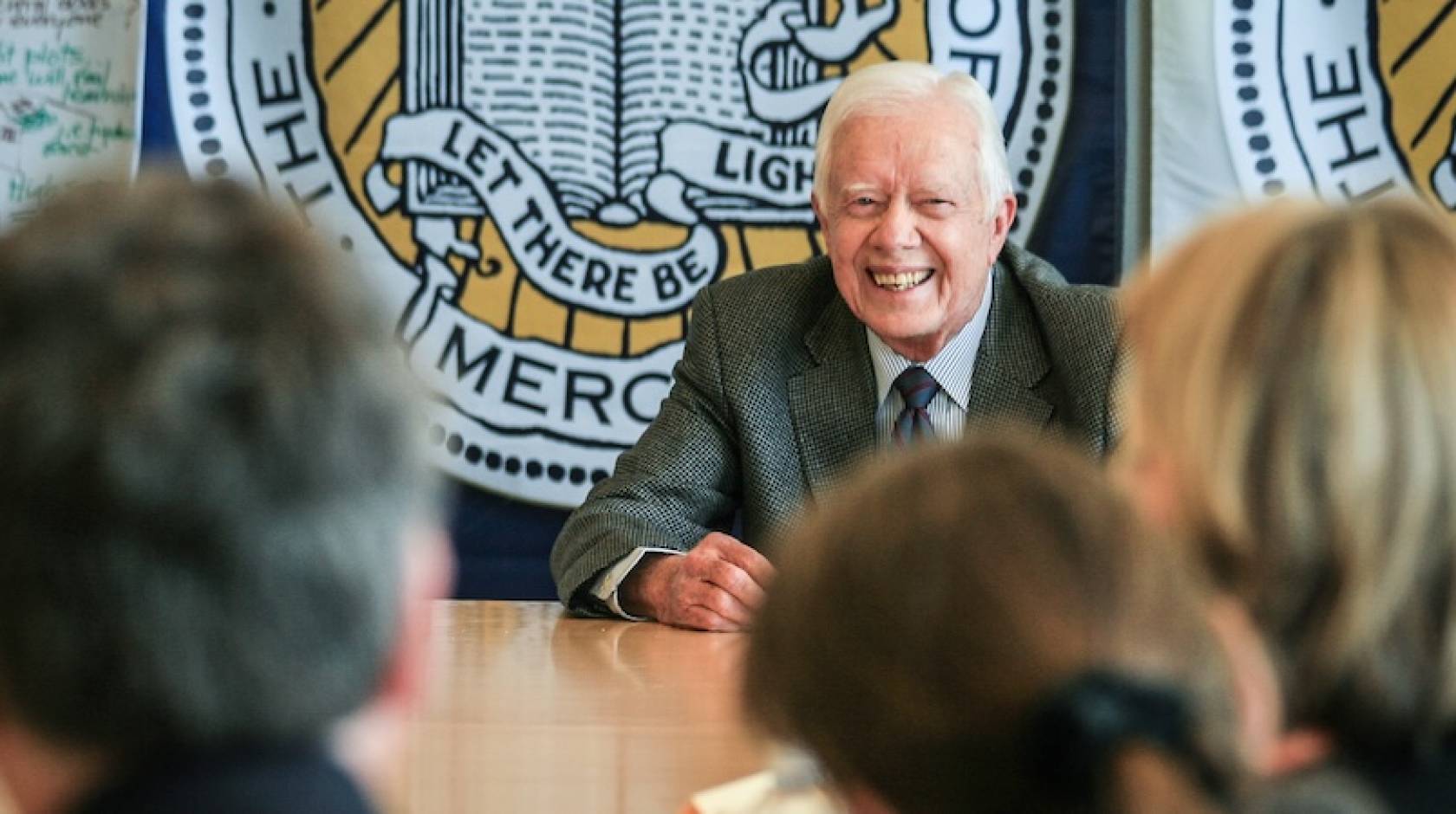 Former President Jimmy Carter, center, smiles broadly as he speaks to an audience around a conference table with the UC Merced official seal behind him