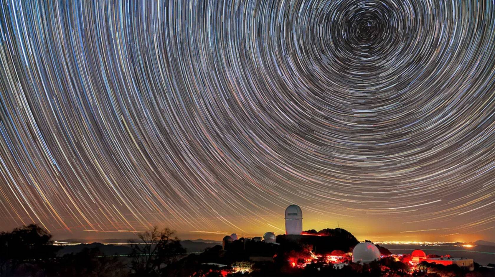 A telescope on a mountain peak at sunset, taken using time lapse to show concentric circles of star trails in the sky