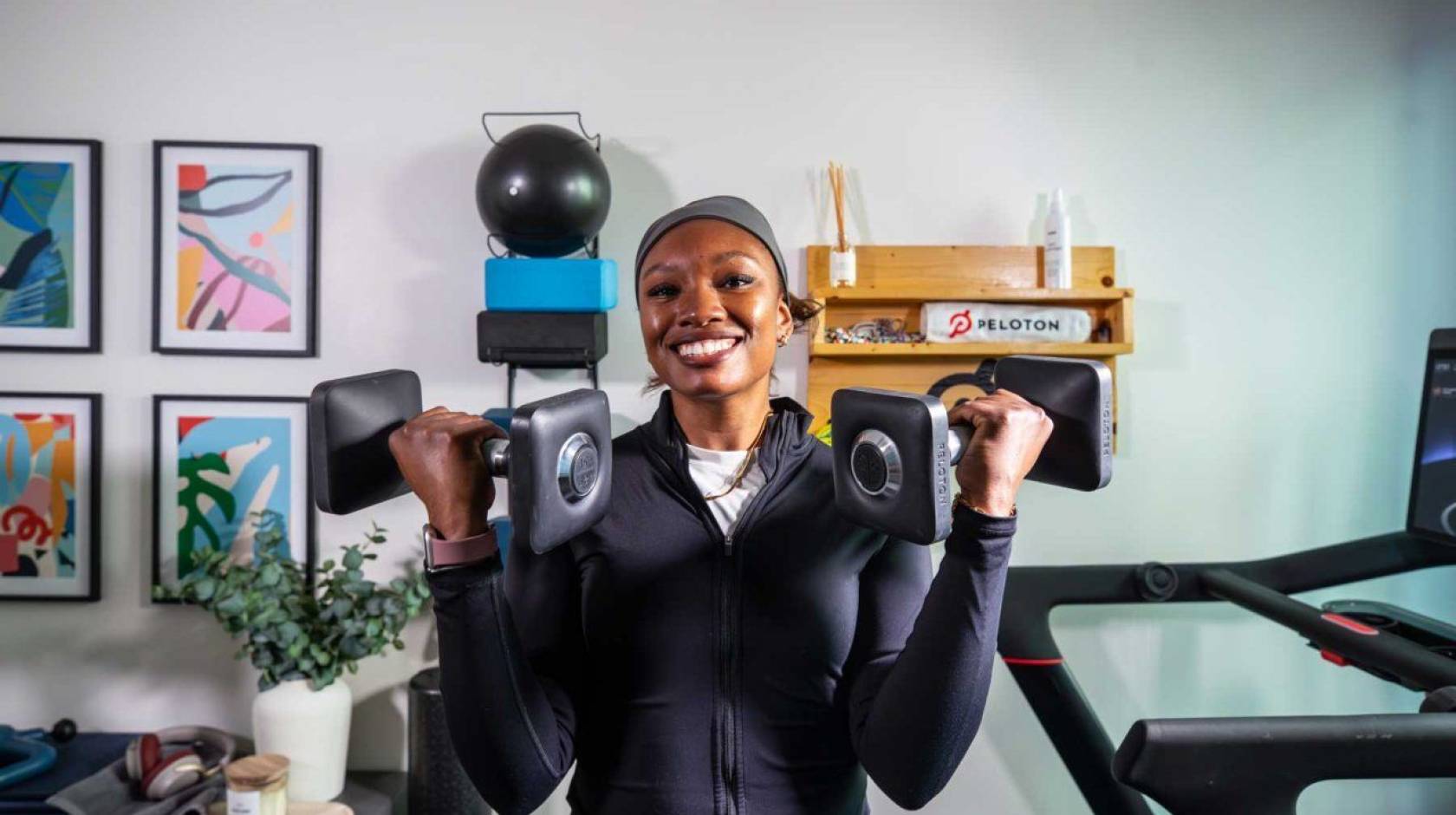 Lauren Patrick smiles at the camera wearing workout attire, holding a dumbbell up in each arm