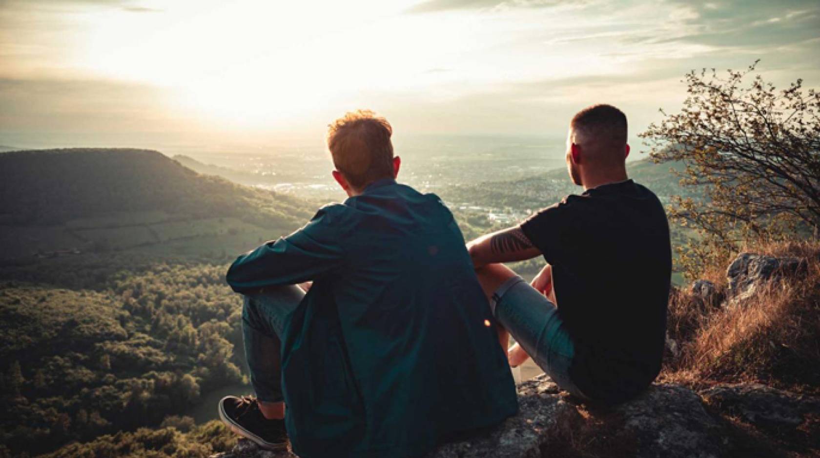 Two men stare down into a sunlit valley