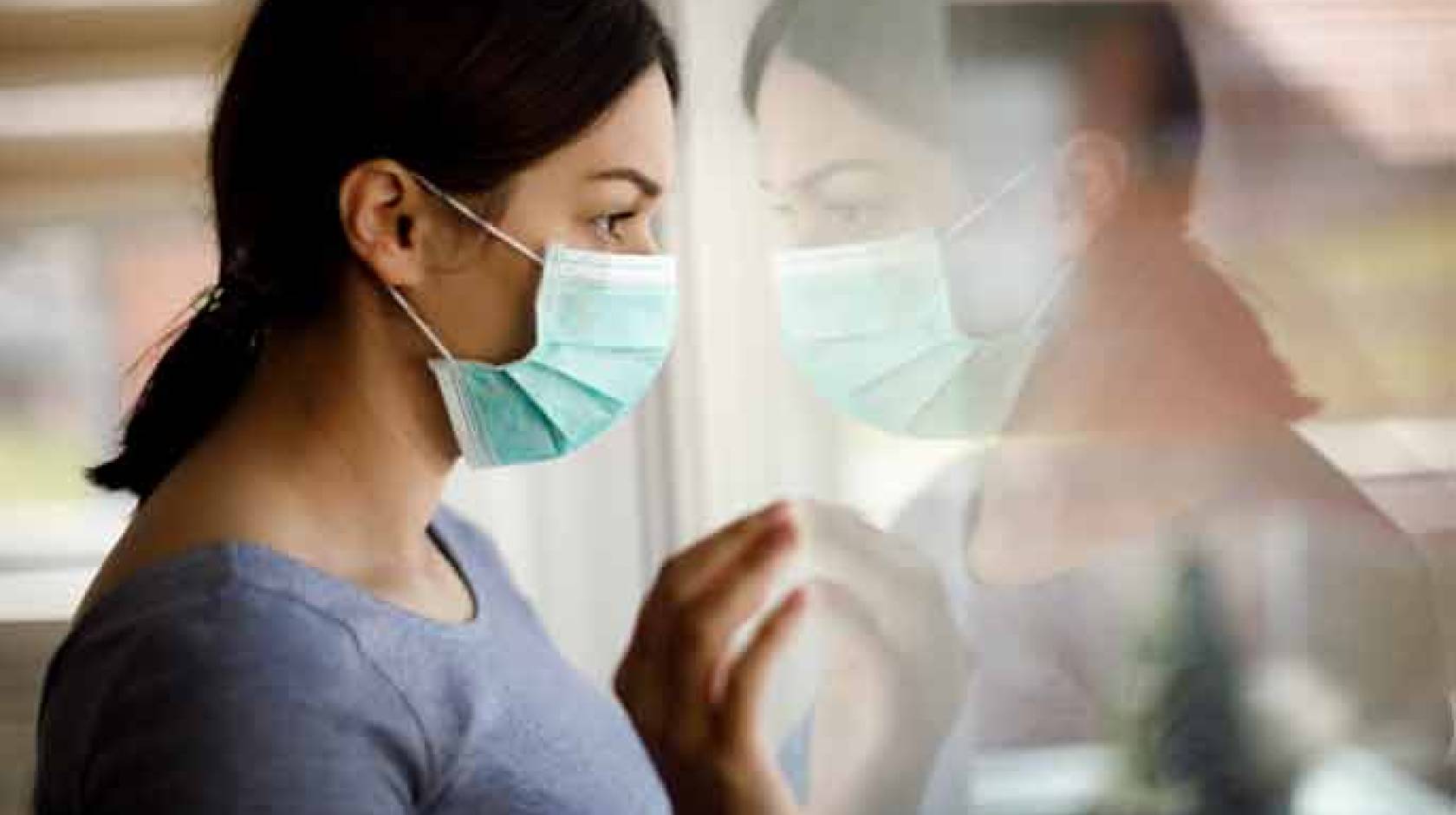 Woman wearing mask looking outside, forlorn