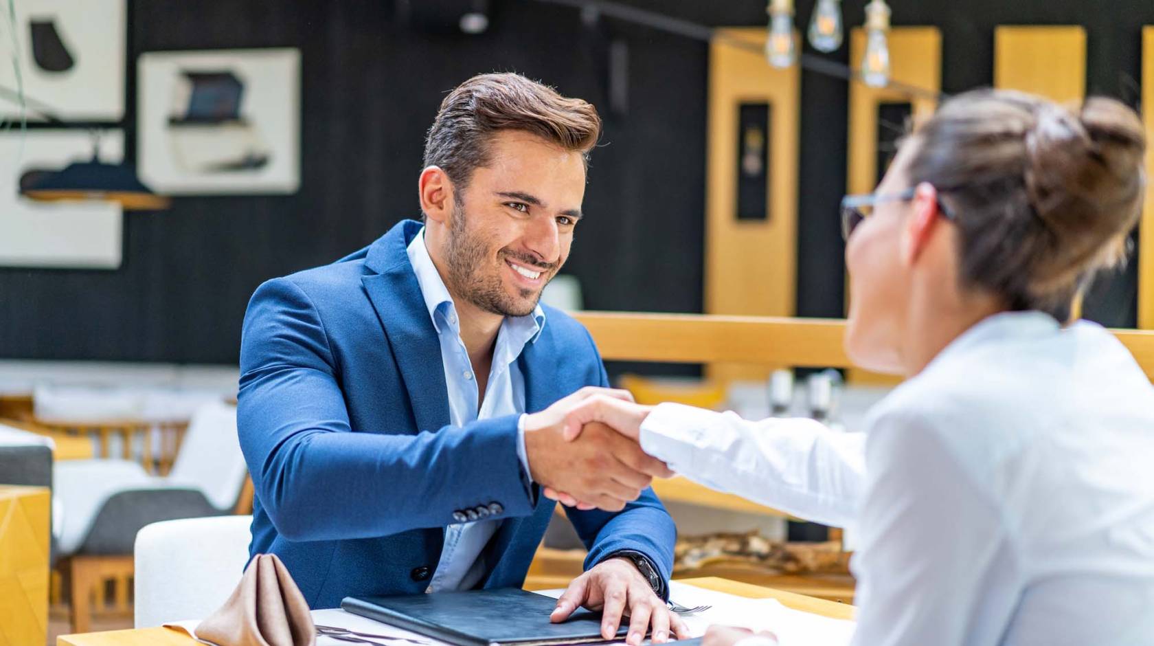 Man smiling and shaking the hand of a woman over a table