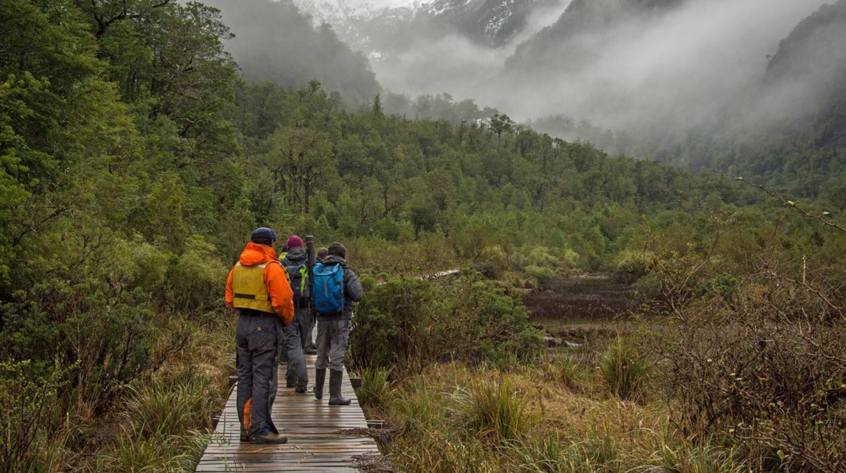 People on a boardwalk in Patagonia looking into foggy valley