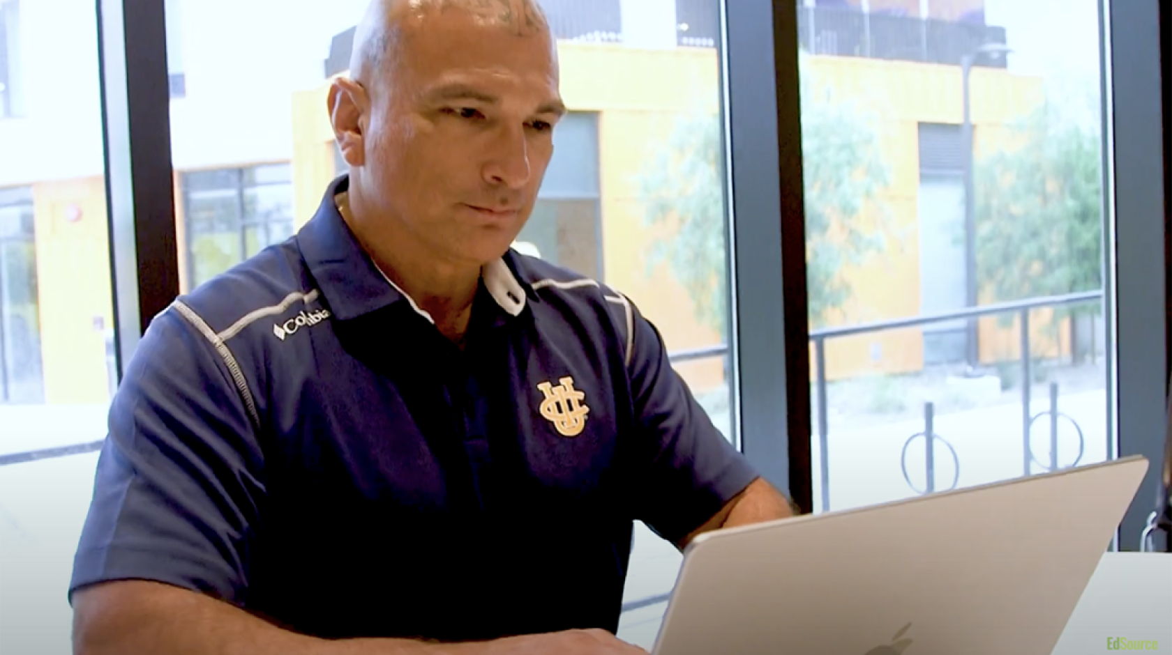 Patrick Acuña, wearing a blue UCI polo and with tattoos on his scalp, types on a laptop.