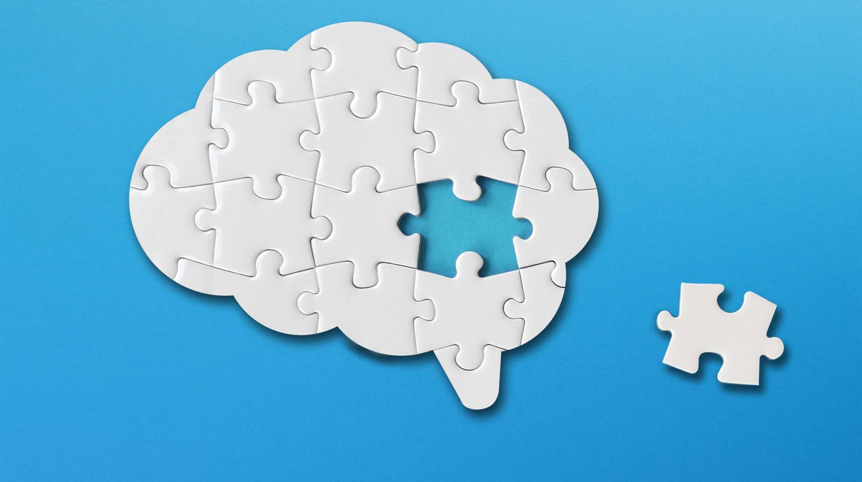 A puzzle of a brain with one piece to the side; puzzle is white on a blue background