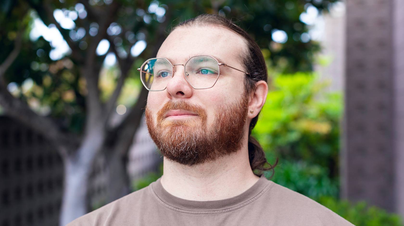 A man with a beard and pony tail wearing a T-shirt and glasses gazing into the distance