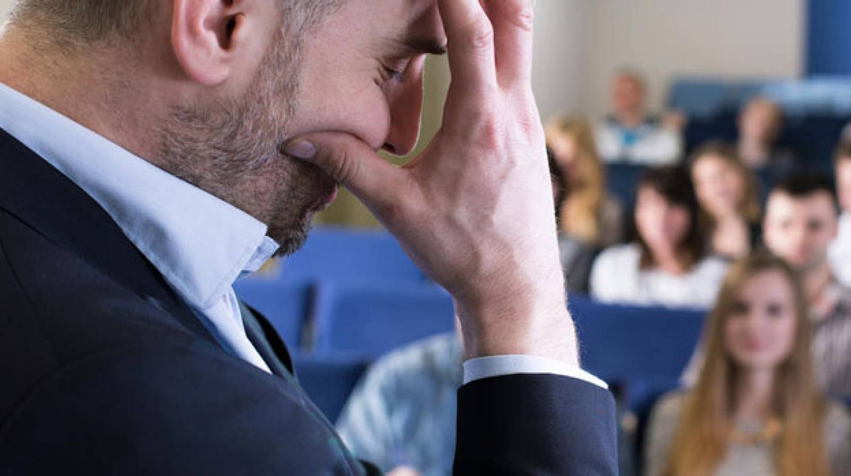 A man in front of a room holding his hand in front of his face in frustration