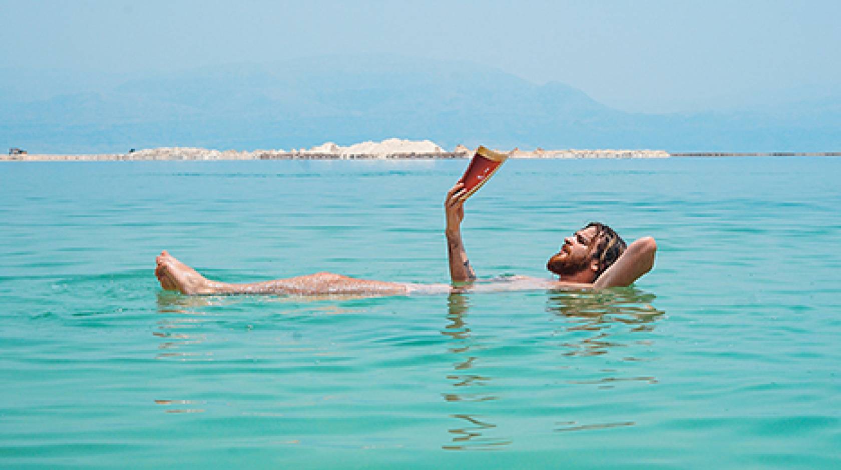 man reads while soaking in a lake