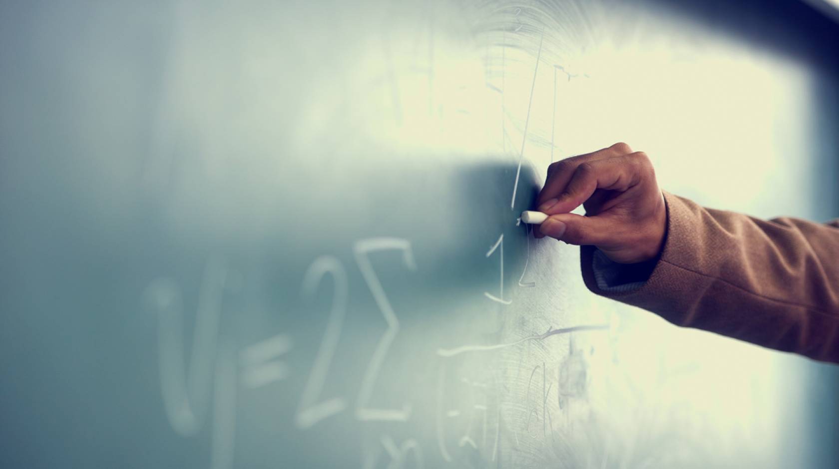 A Black teacher writing on a chalkboard