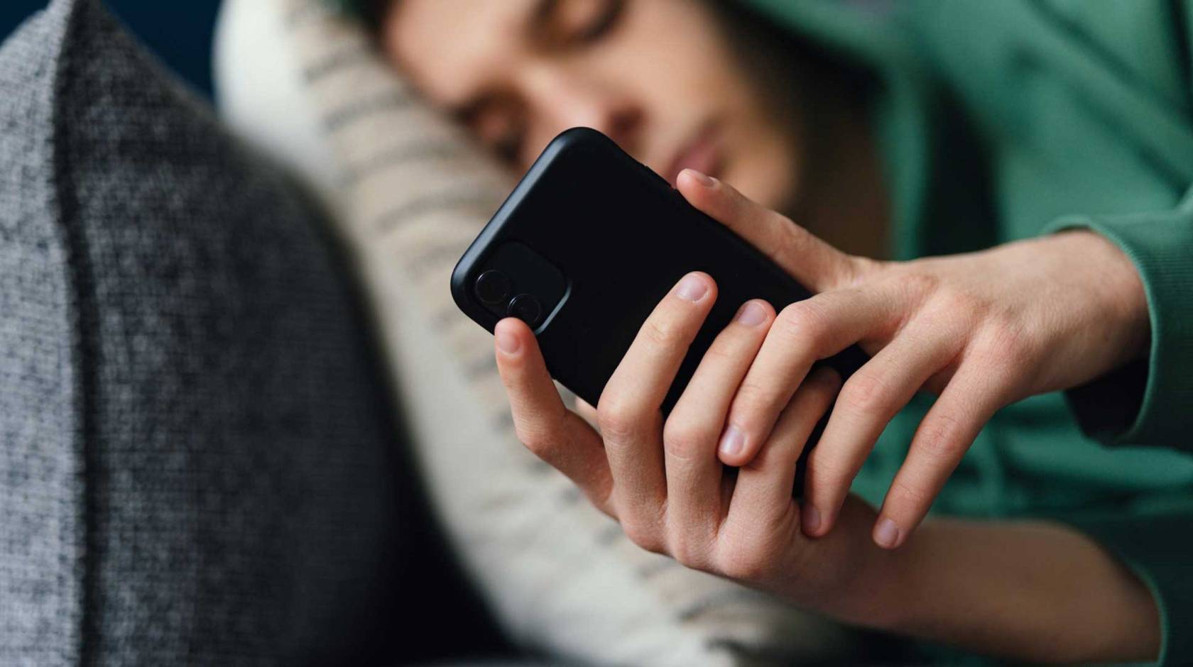 A teen, slightly out of focus, lying on the couch, looking at phone