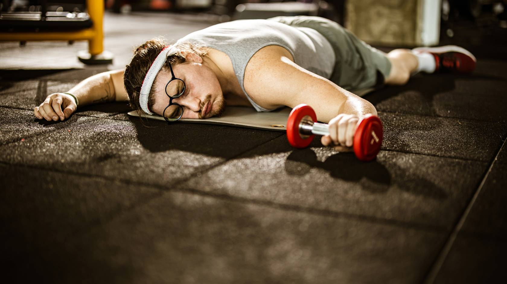 Male athlete lying on the floor, feeling exhausted after sports training with dumbbells in a gym