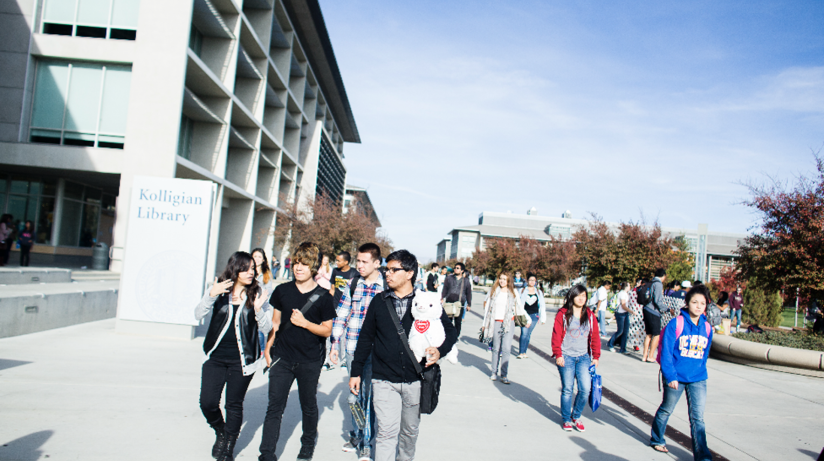 A group of students walking along the UC Merced campus, blue sky in background