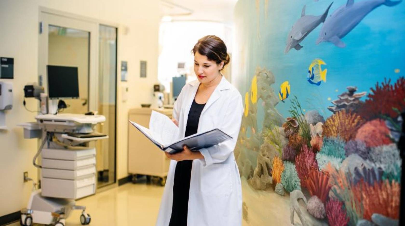 Woman doctor in white coat looks at a medical record with a colorful wall with an undersea mural behind her