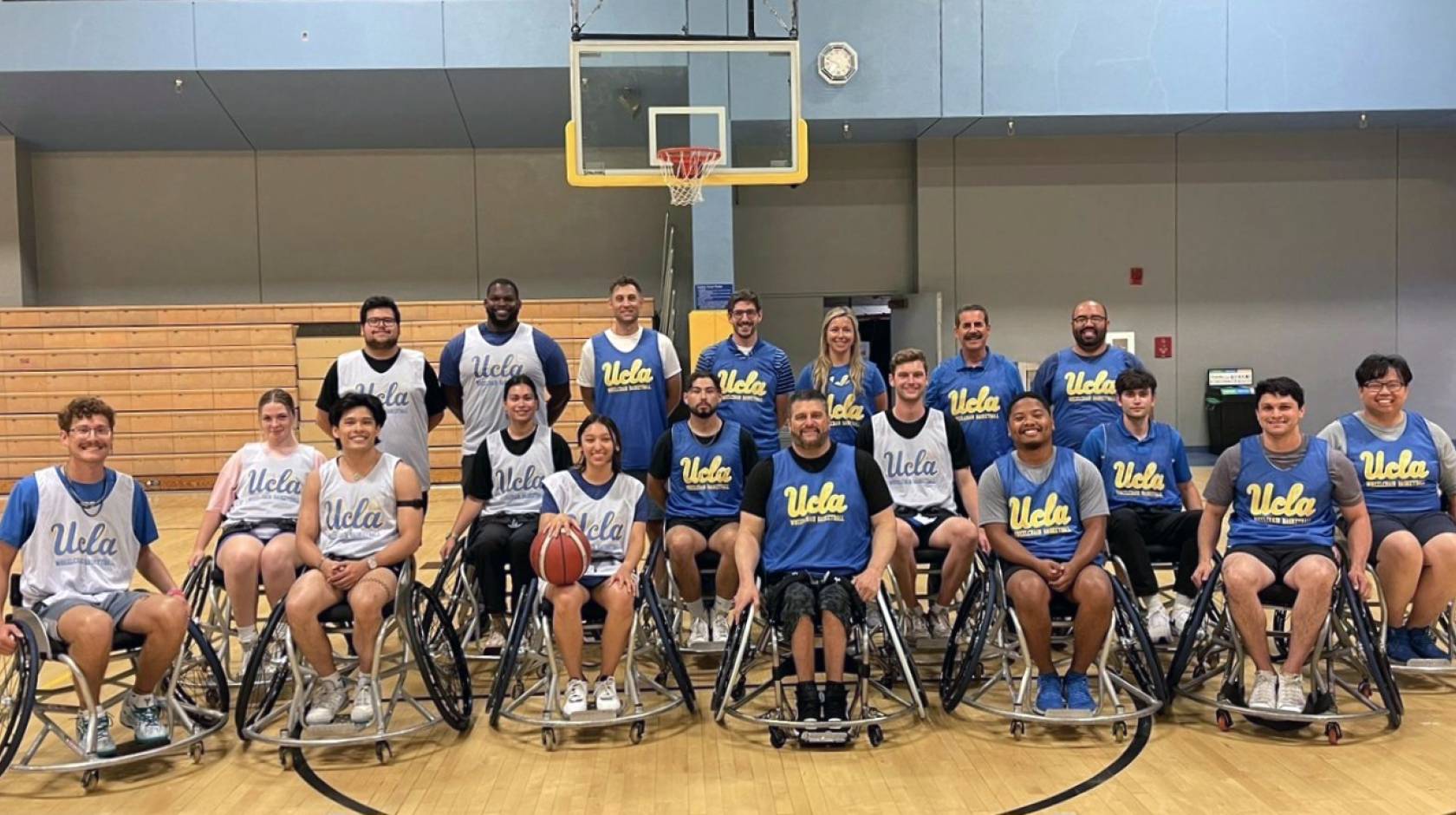 Group photo of the UCLA wheelchair basketball group in front of a basketball net