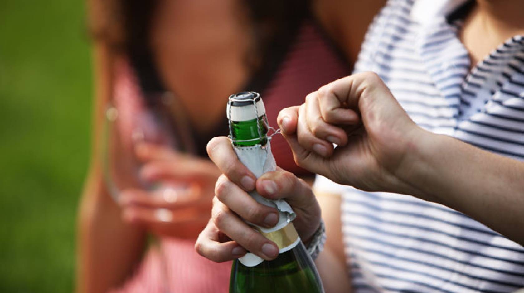 A man opens champagne next to a woman in a park