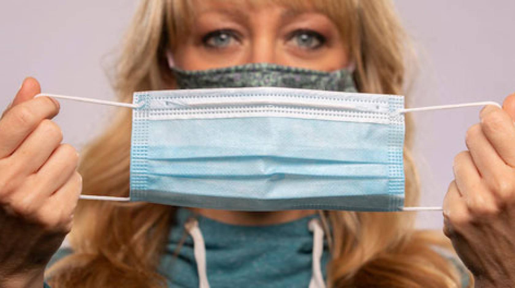 Woman wearing a mask holding up another mask to the camera