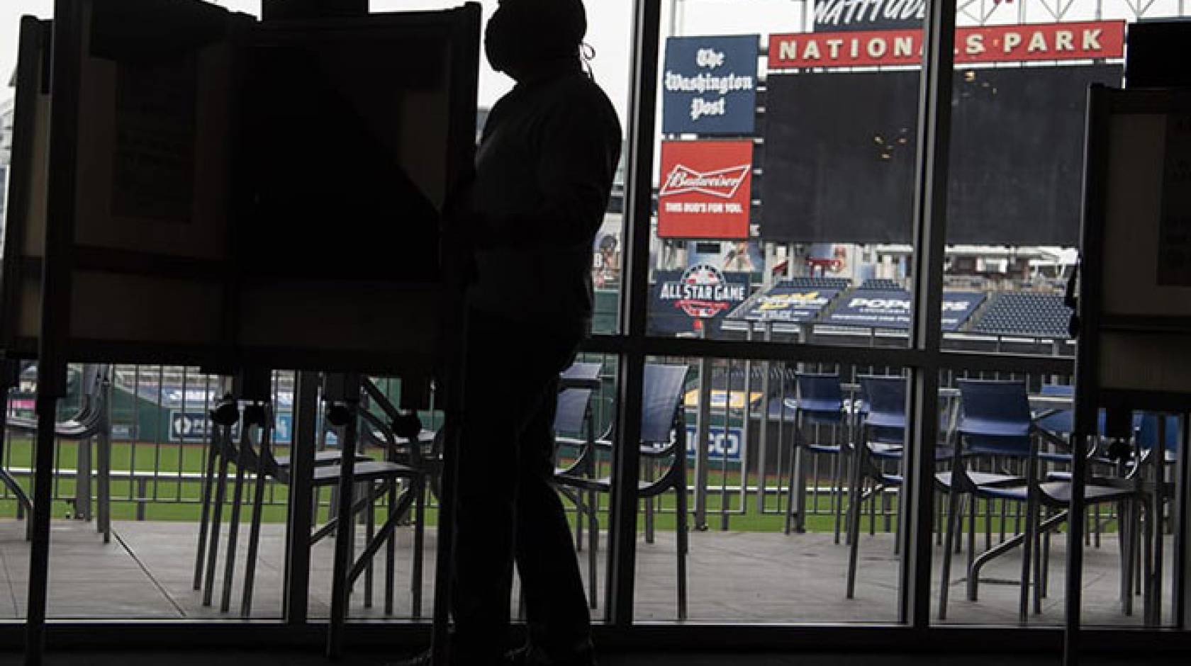 Man at a voting booth, ballpark behind him