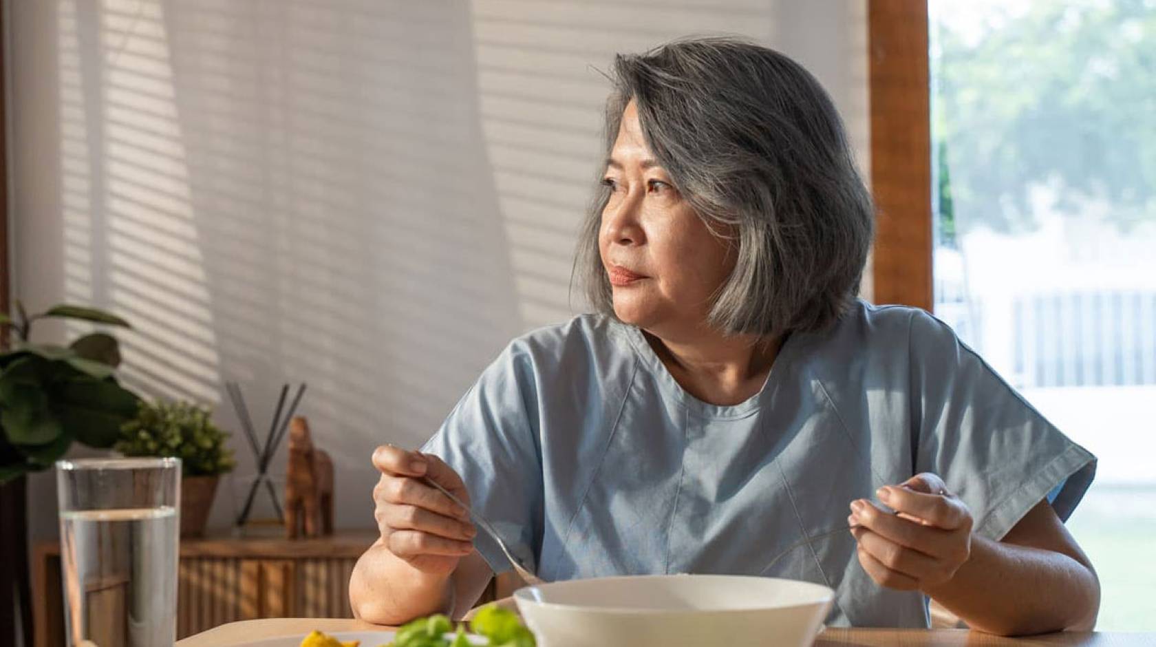 Older Asian woman eating alone, looking wistful