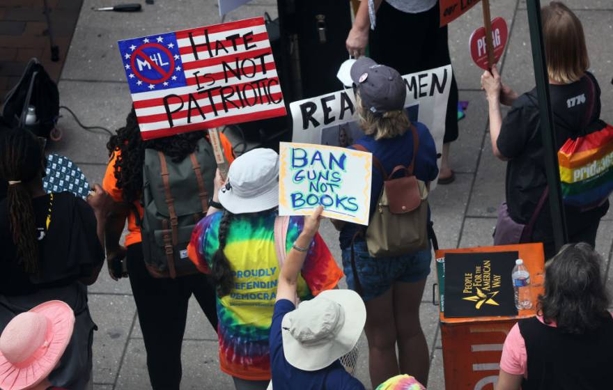 People at a protest holding signs, one reading "Ban guns not books"