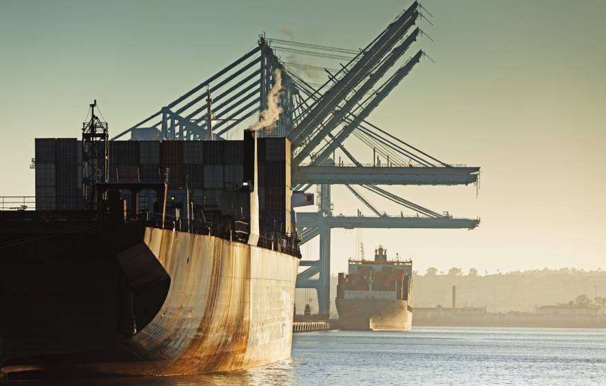 Port emissions Two rusty container ships in a row, one behind, being loaded at a port during the evening
