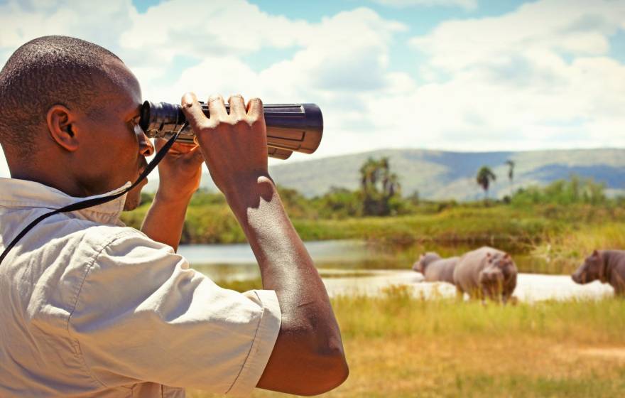 A man in profile looks through binoculars while standing in a field