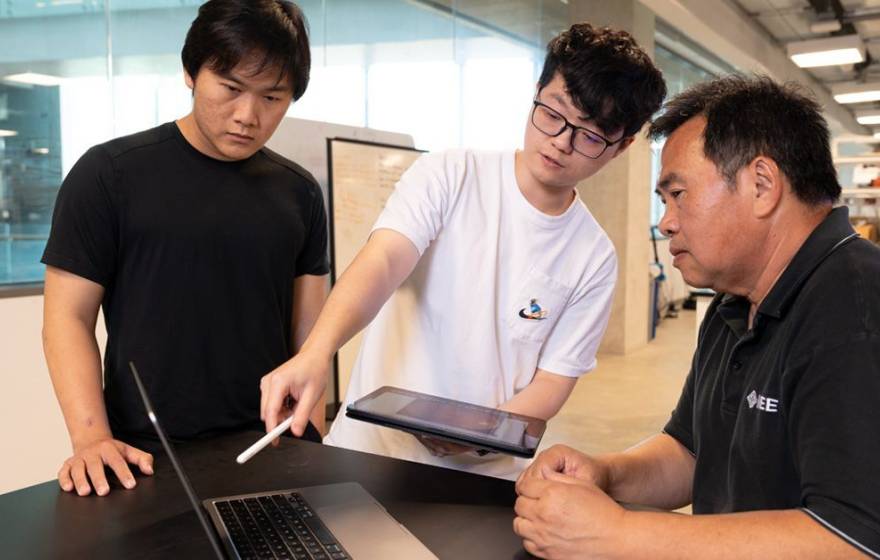 Two students and a professor look at a computer