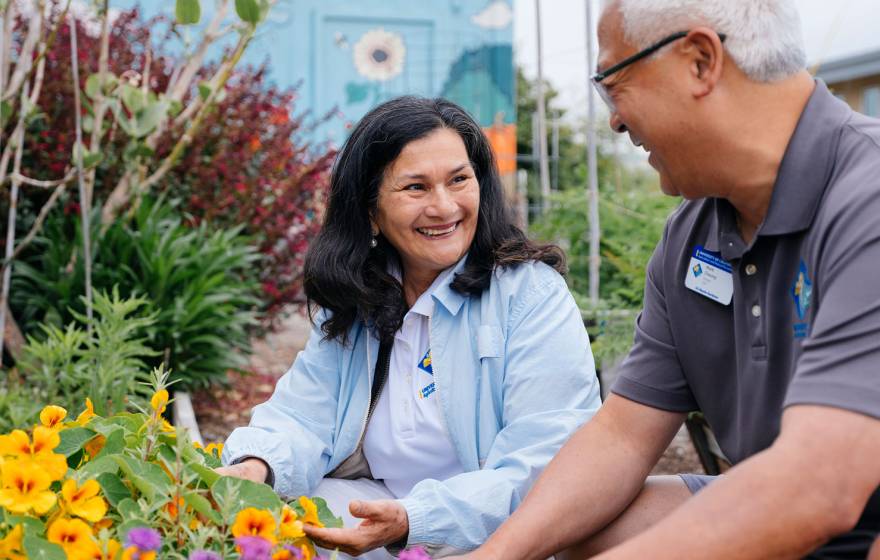 A man and woman smile while tending to a colorful garden.