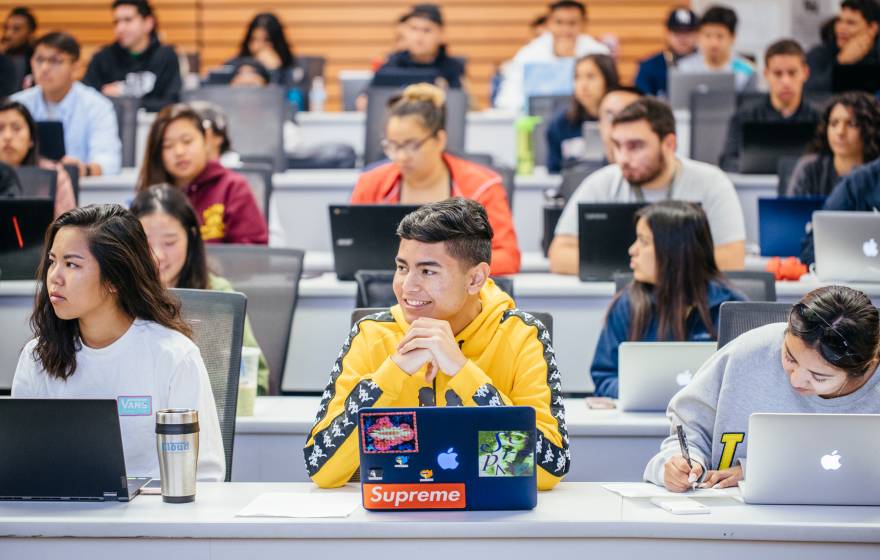 students sitting in a lecture hall listening and engaged, each with an open laptop