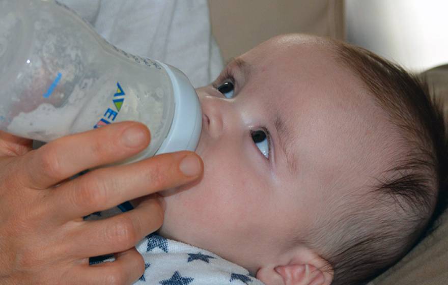 Baby drinking from a bottle looking up at person feeding