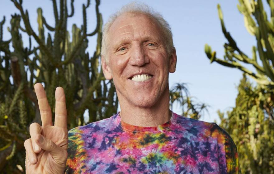 Bill Walton flashes a peace sign while wearing a tie-dyed shirt