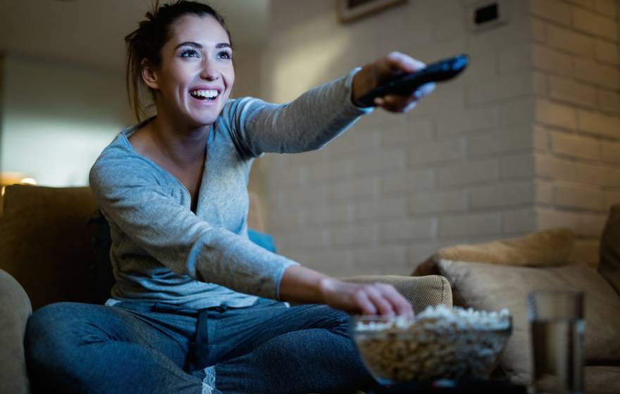 A young woman smiling holding a remote and eating popcorn