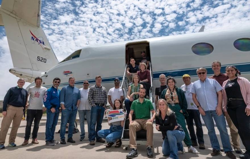 About 20 people gather for a photo on an airport tarmac, in front of a small jet