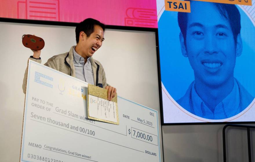 A man smiles while holding a trophy and a giant check for $7,000