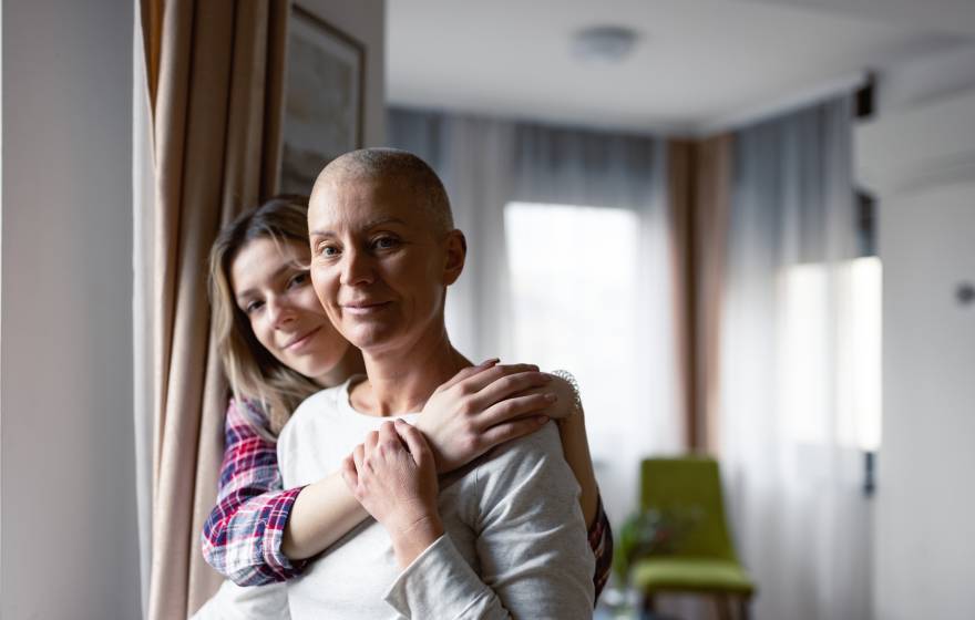 A grown child holds her mother, who has little hair on her head